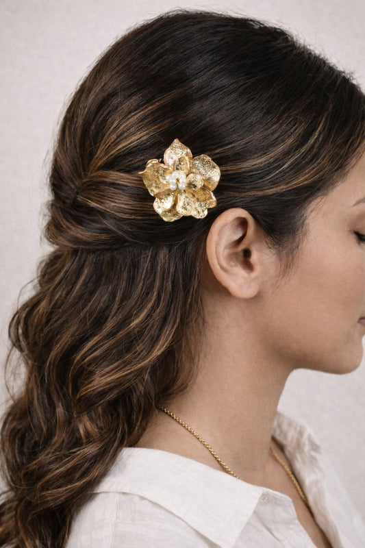 Woman with styled hair featuring a gold flower accessory against a neutral background